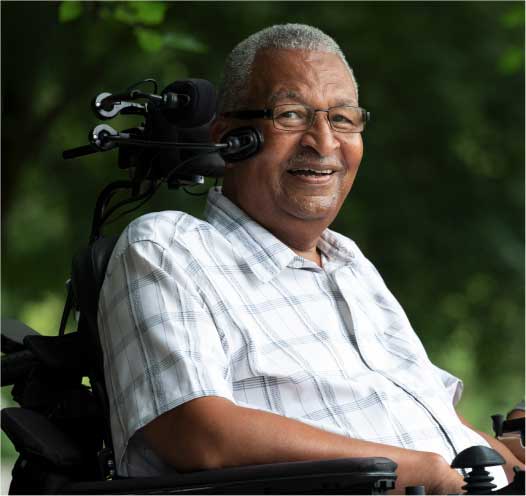 An oversized human hand holds a mouse next to rack of filled test tubes in a lab.